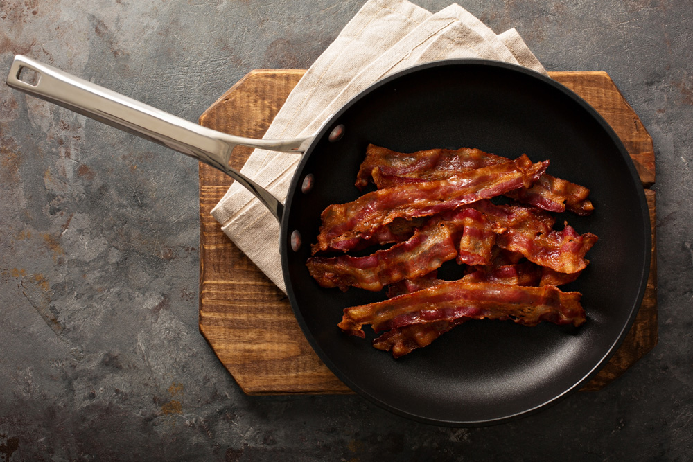 Photo de bacon grésillant dans une poêle en fonte sur un plat de service en bois