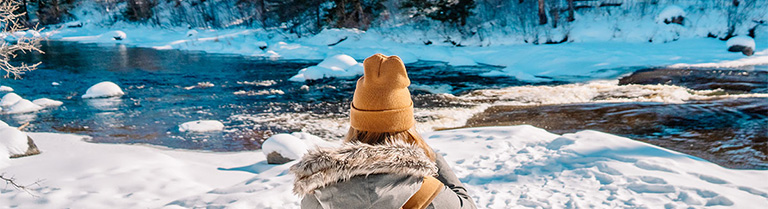 the back of a person standing in the snow in front of a river and treeline